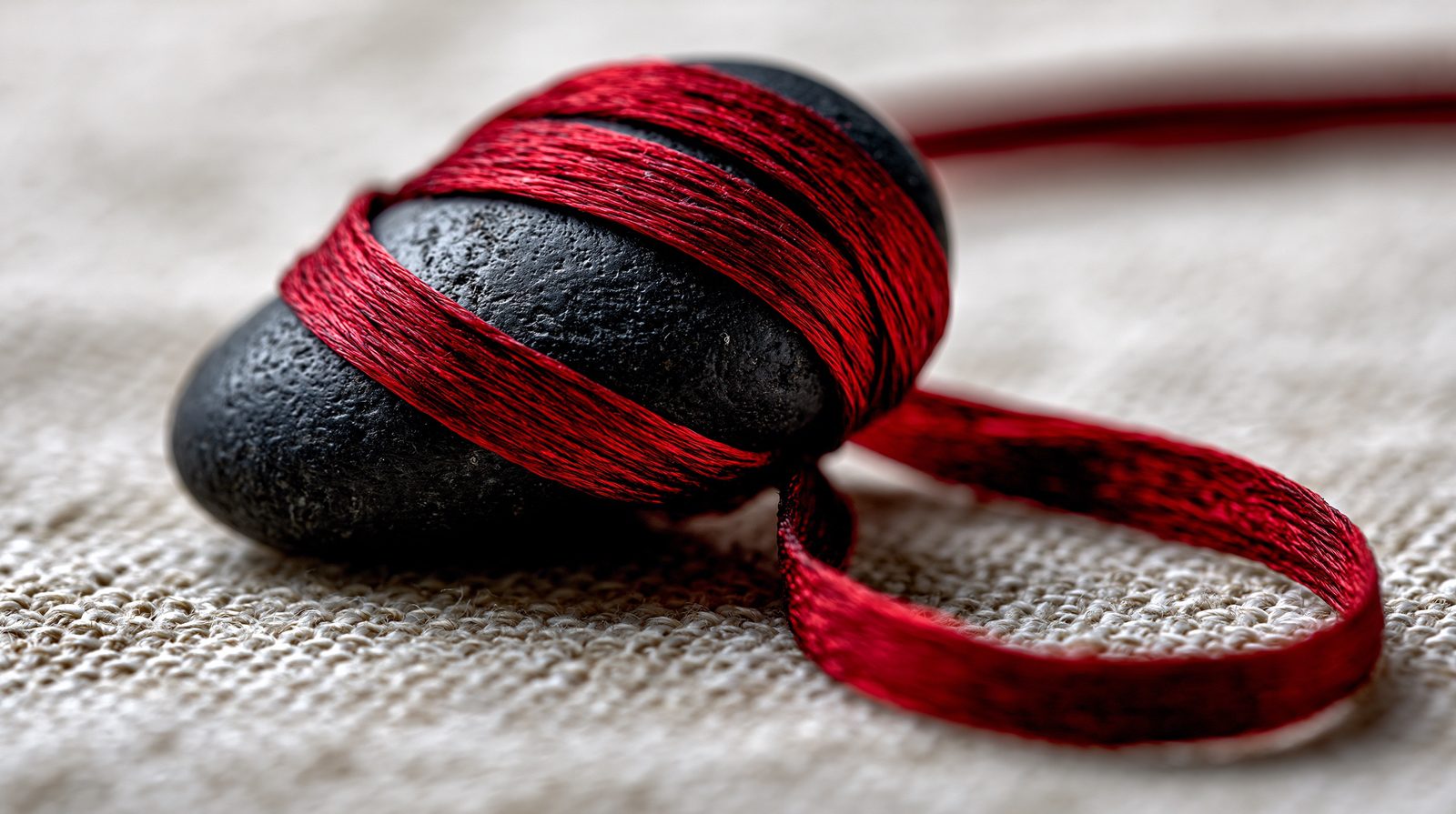 A red thread wound around smooth black stones on linen